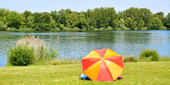 Badestelle an einem Fluß mit Person unter Sonnenschirm im Vordergrund